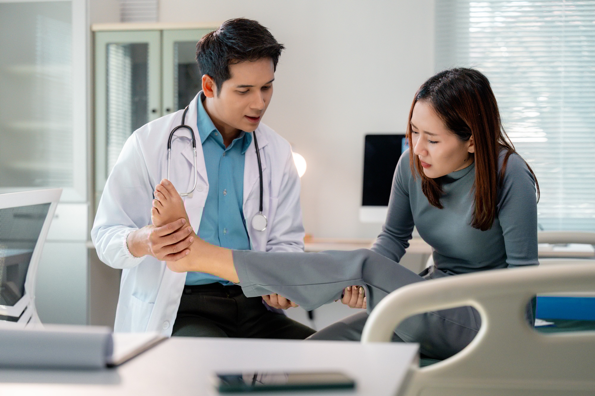 Doctor examining injured foot of female patient sitting on hospital bed